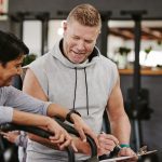 Cardio, personal trainer and senior woman, gym fitness checklist, progress or writing exercise results. Coaching, lose weight and sports professional helping elderly person on running machine workout.