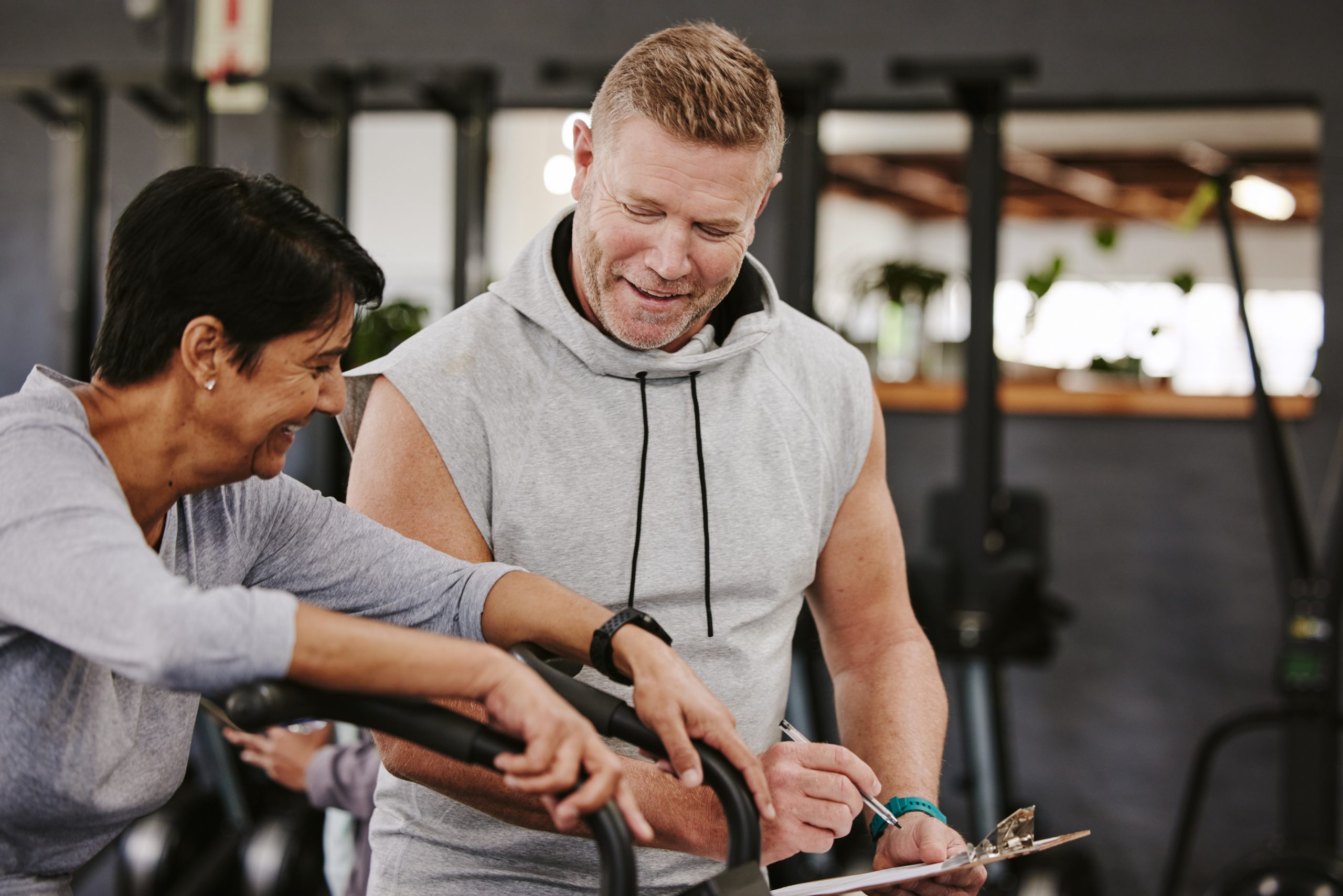 Cardio, personal trainer and senior woman, gym fitness checklist, progress or writing exercise results. Coaching, lose weight and sports professional helping elderly person on running machine workout.
