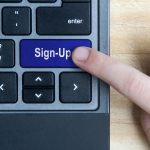 Top view of hand pressing sign-up button on laptop keyboard.